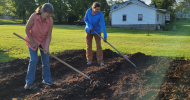 Two women using hoes to prepare soil for a garden.